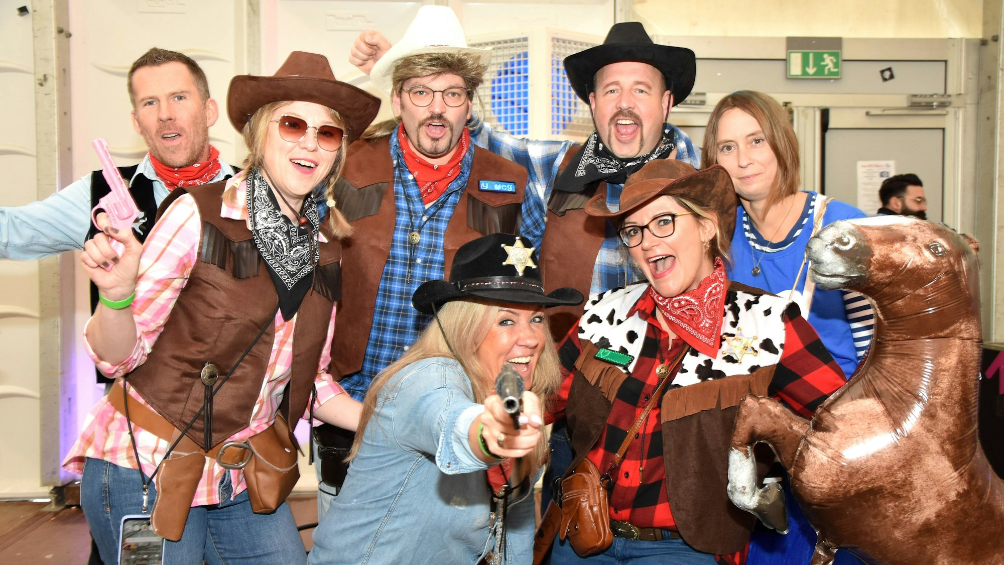 Als Cowboys verkleidete Jecke in einem Festzelt halten einen Ballon in der Form eines Pferdes.