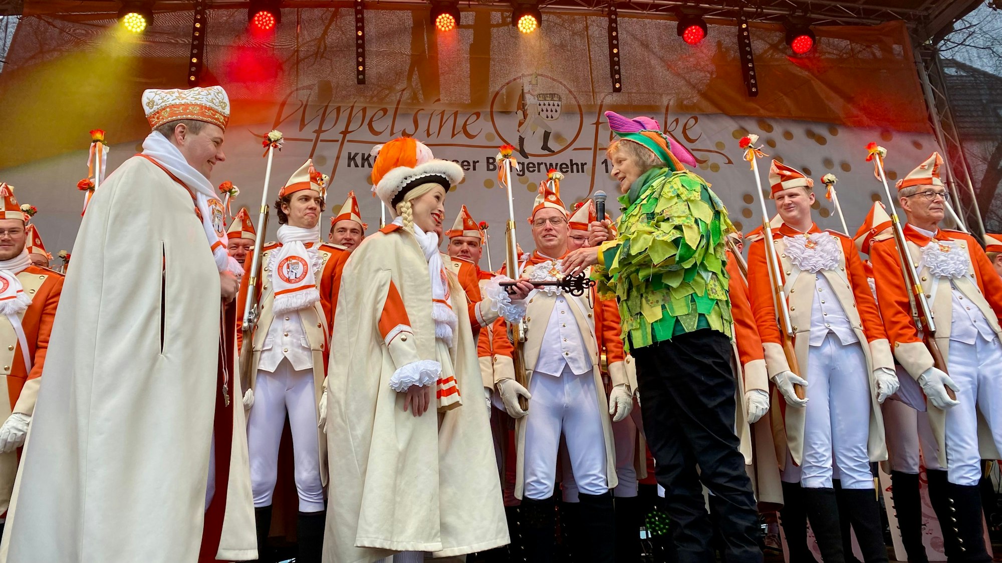 Eine mit Schirmen und Regencapes ausgestattete Menschenmenge ist zu sehen.