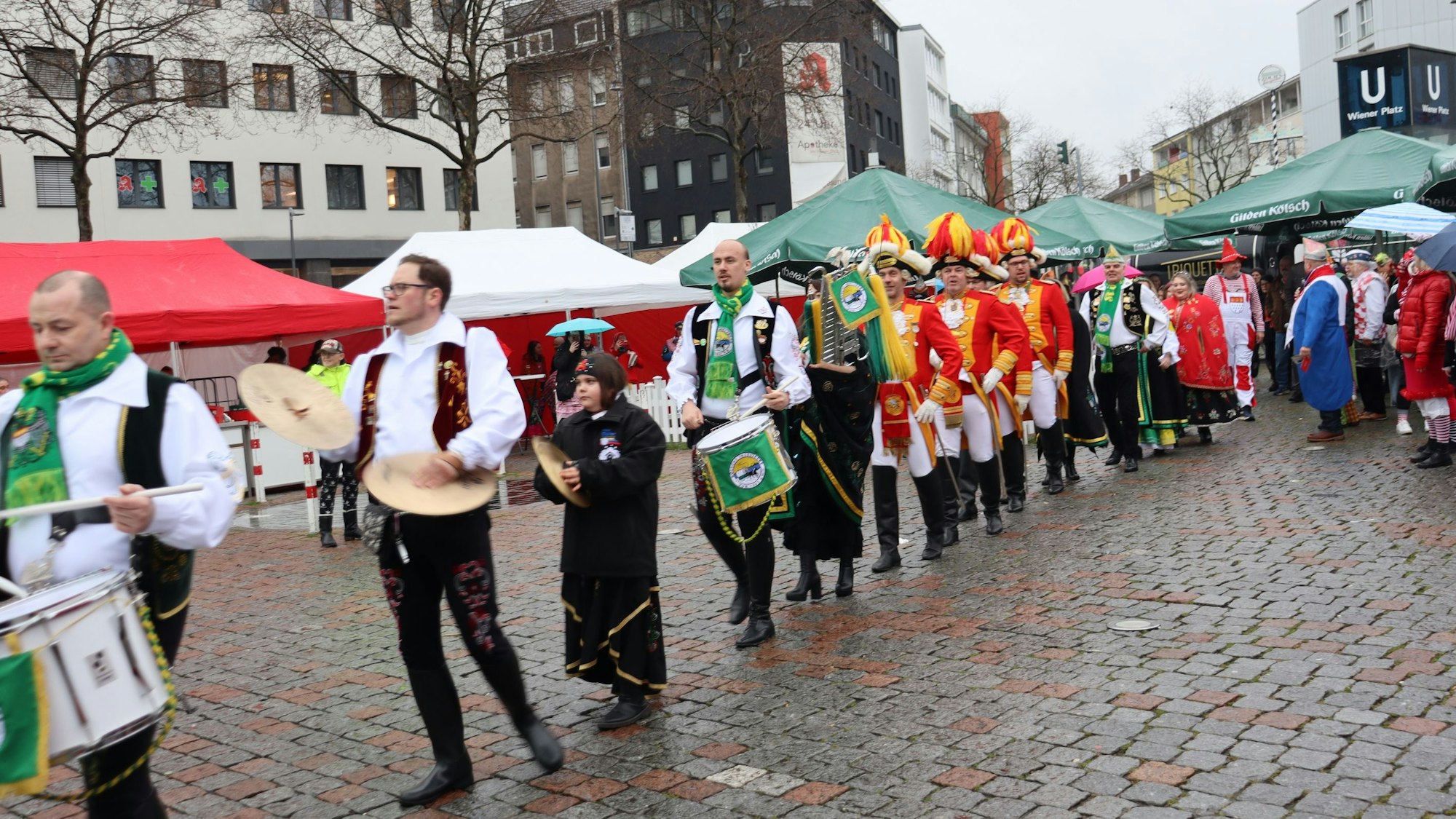 Viele Menschen mit Trommeln und in Uniformen laufen hintereinander über einen Platz.