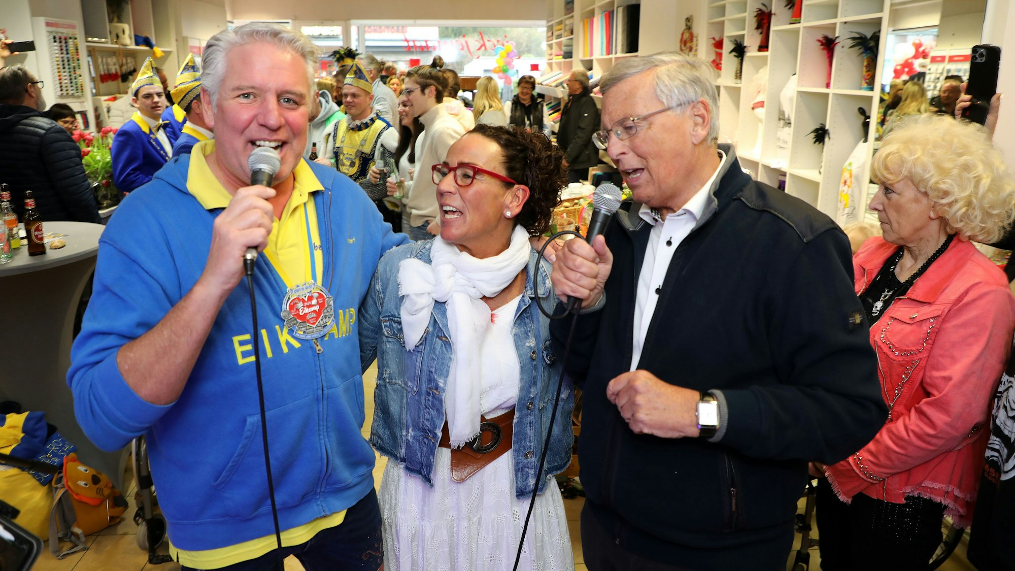 Zwei Männer singen mit Mikros, in ihrer Mitte haben sie eine Frau untergehakt.
