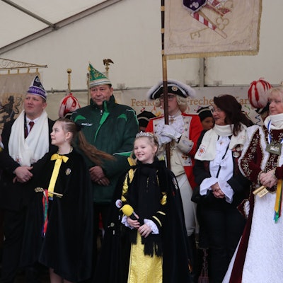 Auf dem Bild ist Frechens Bürgermeisterin und die beiden Prinzessinnen zu sehen. Hinter ihnen stehen viele karnevalistisch verkleidete Personen.