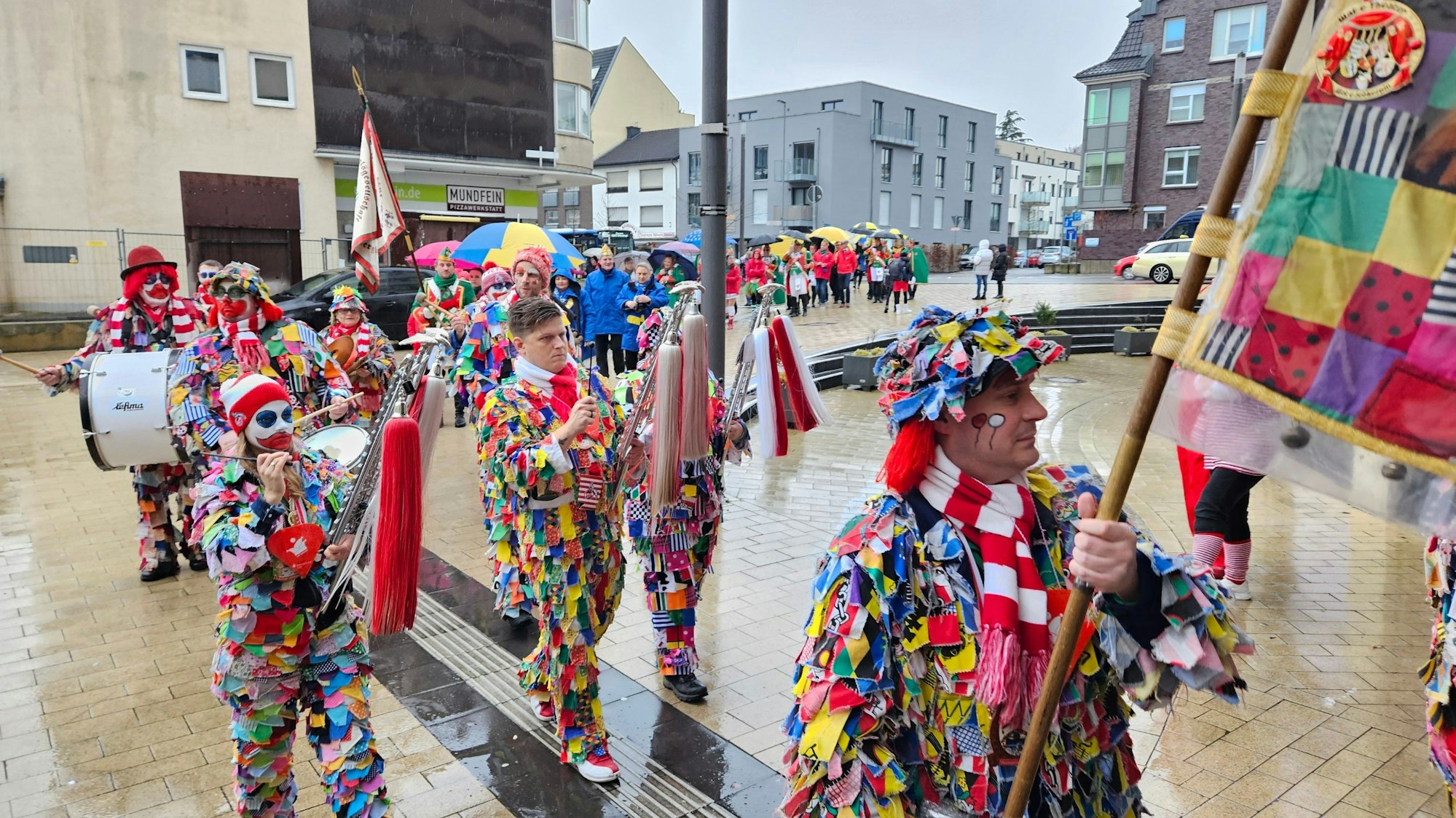 Bunt kostümierte Jecken mit Musikinstrumenten ziehen durch eine Innenstadt.