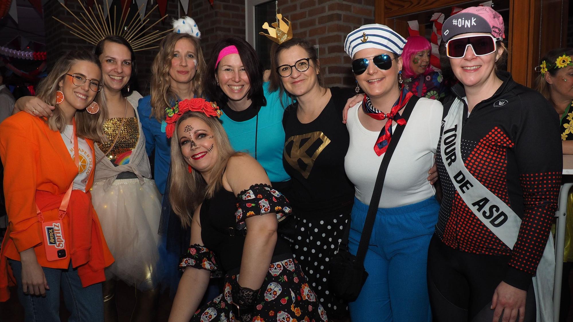 Acht bunt kostümierte Frauen lächeln in die Kamera.