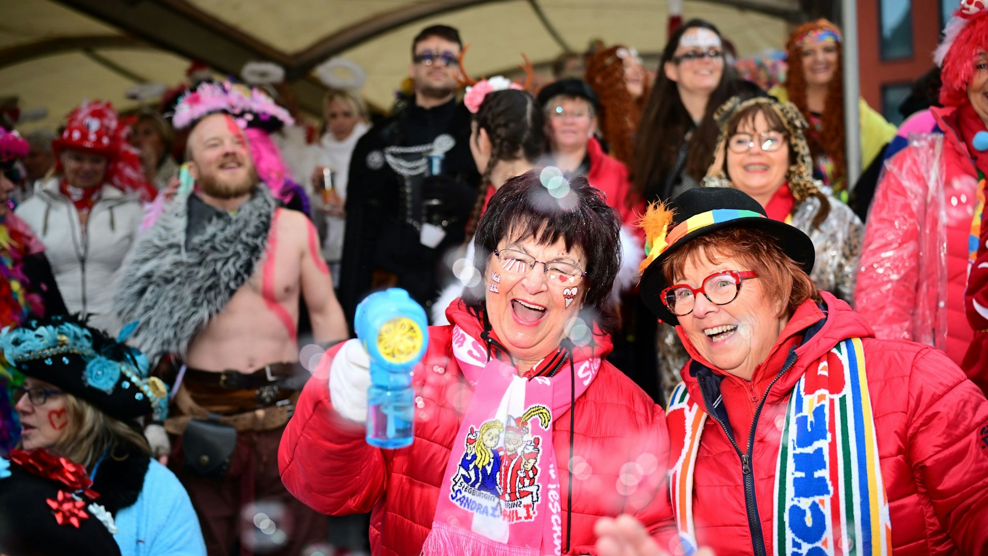 Verkleidete Menschen, im Hintergrund ist ein Mann mit nacktem Oberkörper.