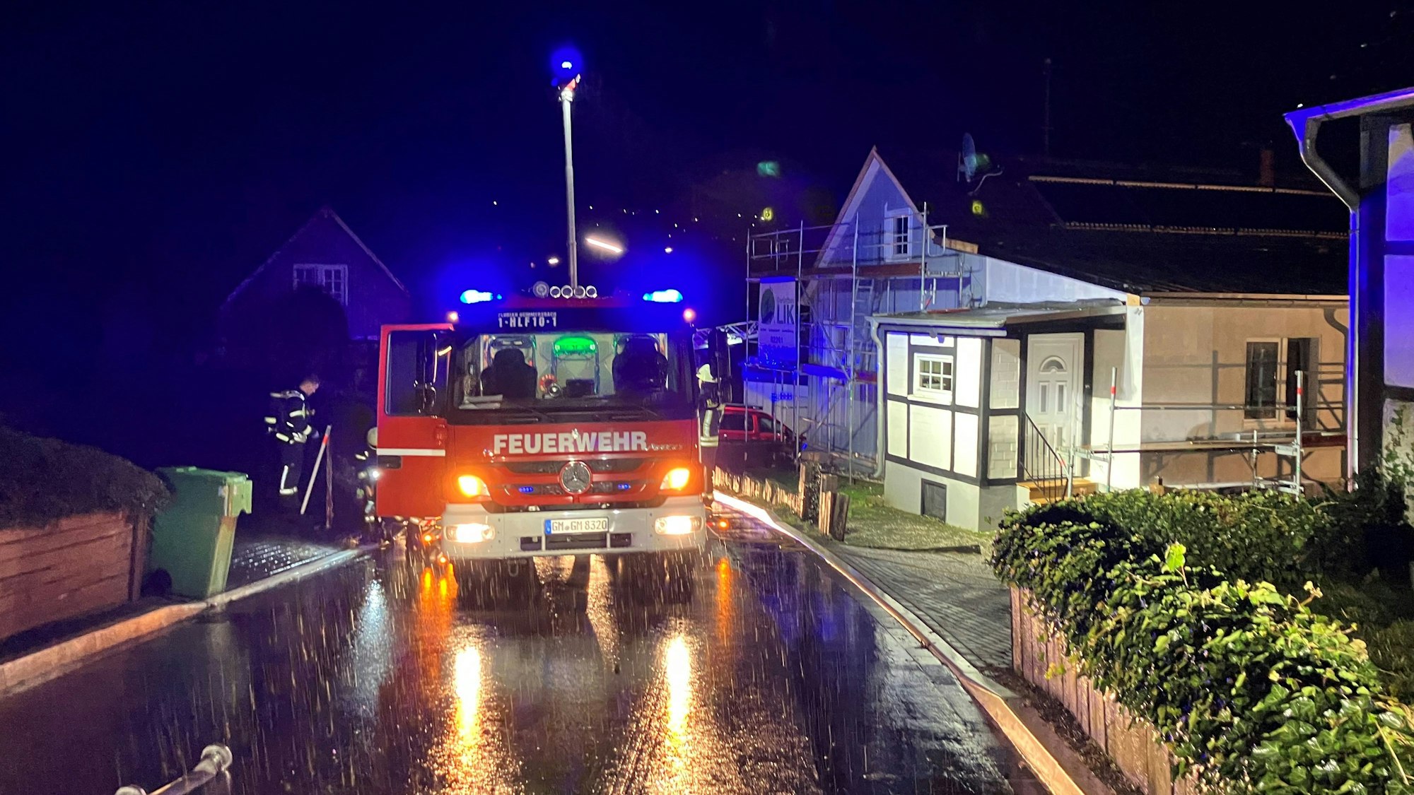 Ein Feuerwehrwagen mit eingeschaltetem Blaulicht steht vor einem Fachwerkhaus.