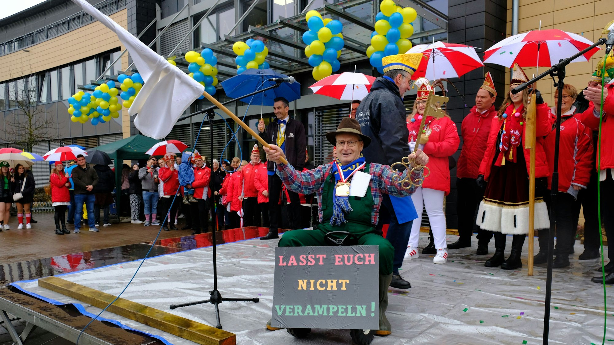 Bürgermeister Hans-Peter Schick sitzt auf einem Spielzeugtrecker und schwenkt die weiße Fahne. In der linken Hand hält er den Stadtschlüssel, den er an die Jecken abgibt.