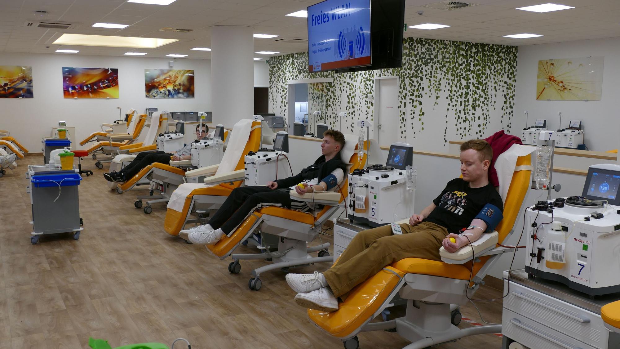 Blick in einen Raum, in dem viele Menschen Blut spenden.