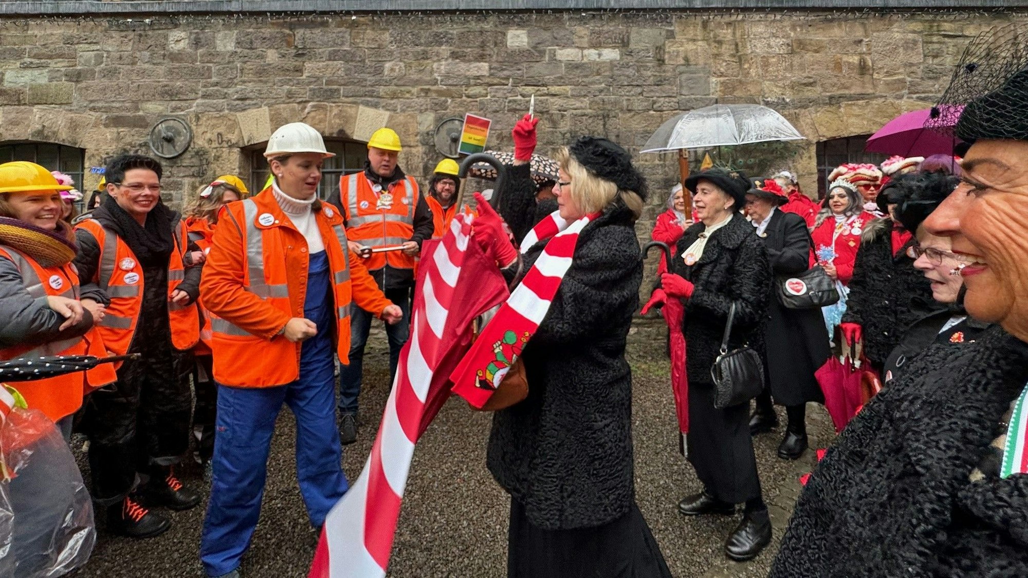 Vor dem Engelskirchener Rathaus ist Flatterband gespannt. Die Mitarbeitenden stehen als Arbeiter auf der einen Seite. Viele verkleidete Frauen auf der anderen.