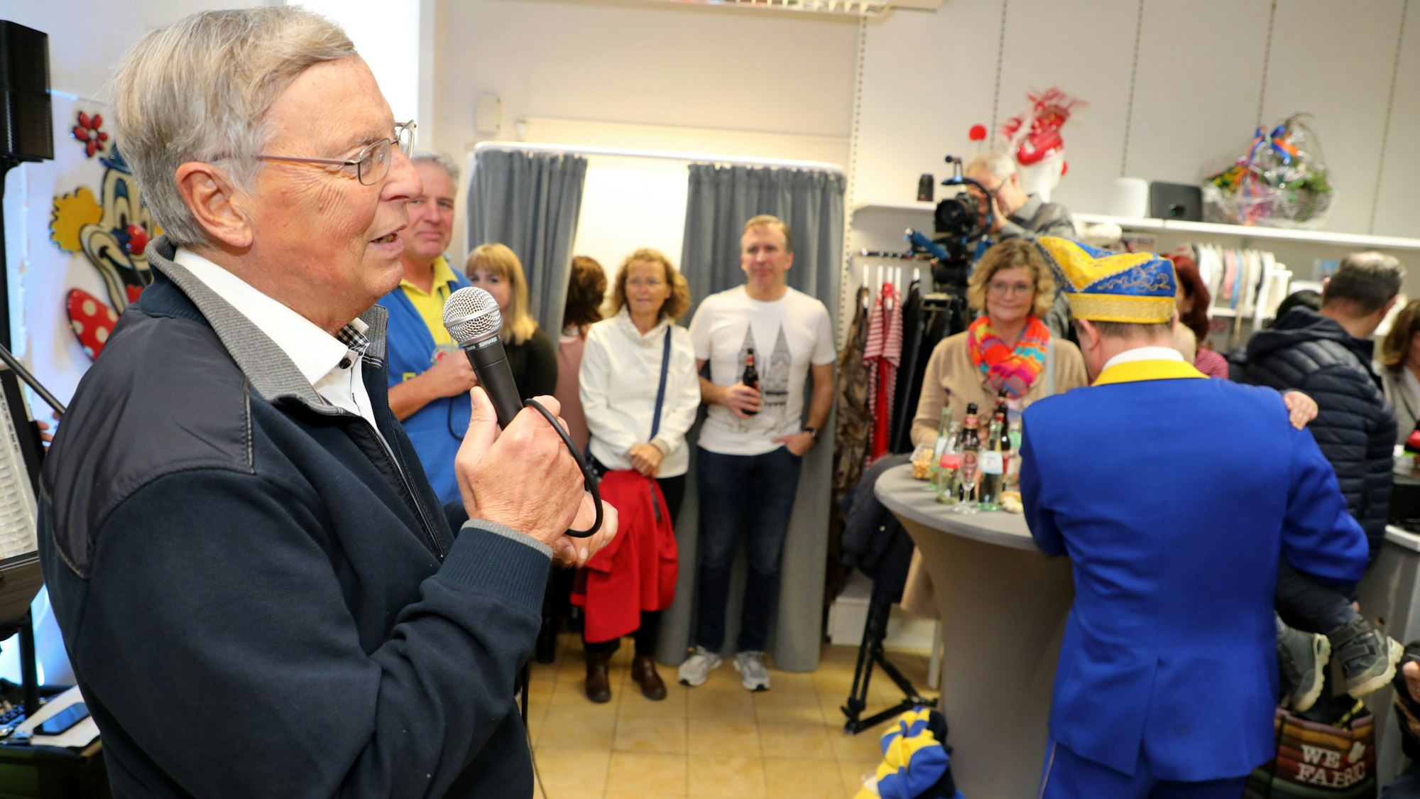 Politiker Wolfgang Bosbach spricht mit einem Mikro zu den Eröffnungsgästen im Laden „Jeck jemaat“ in Bergisch Gladbach-Heidkamp.
