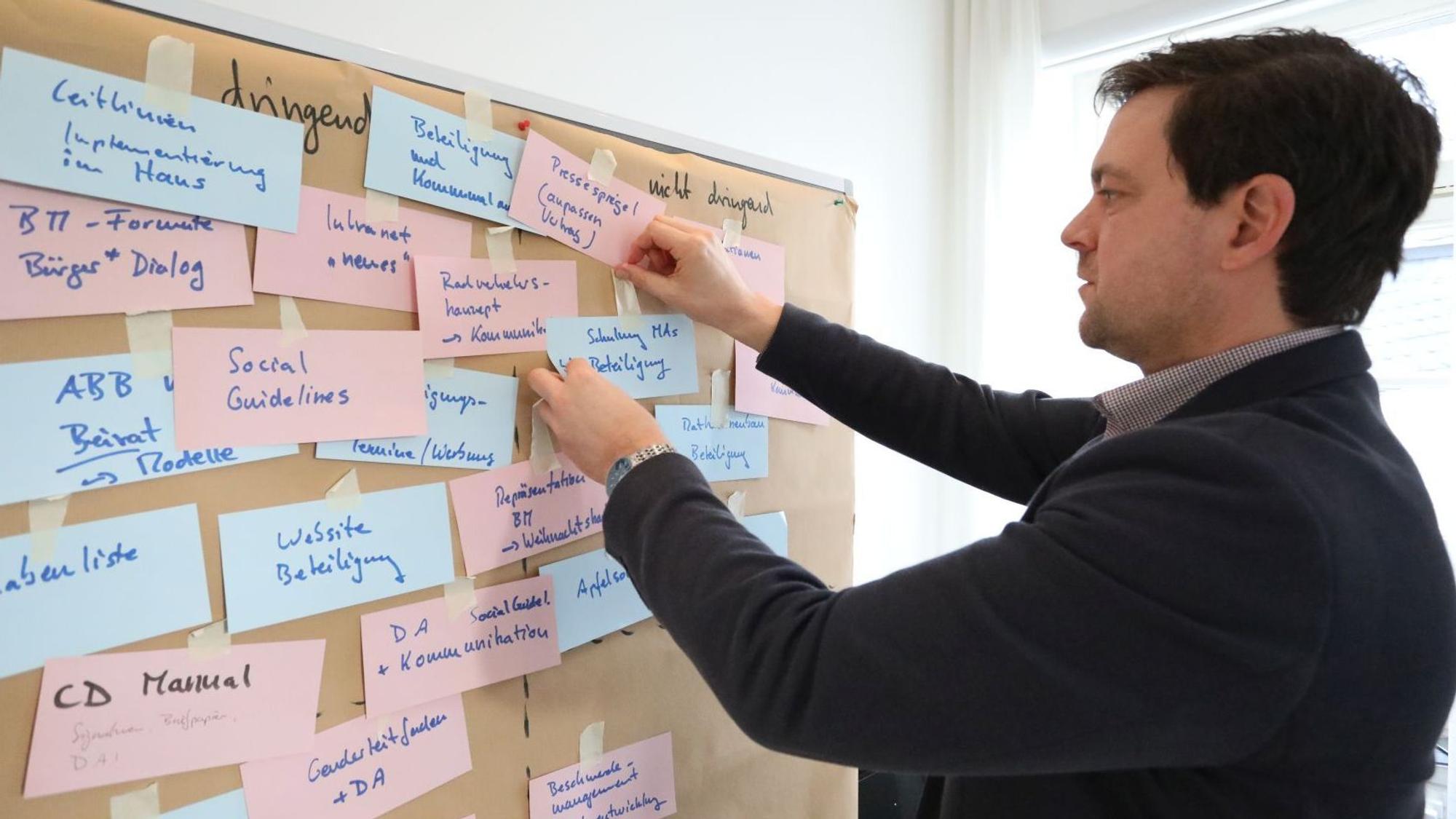 Ein Mann heftet Notizen an eine Pinwand.