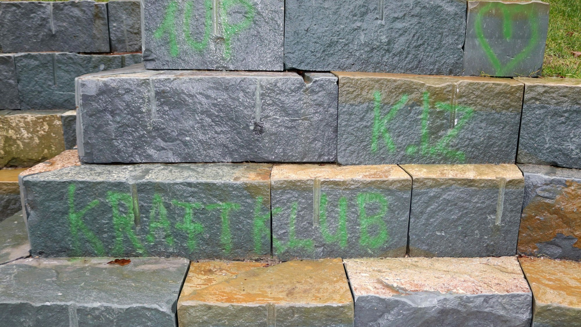 Das Bild zeigt die geschmierten Aufschriften mit den Bandnamen „Kraftklub“ und „K.I.Z“ auf den Natursteinen.