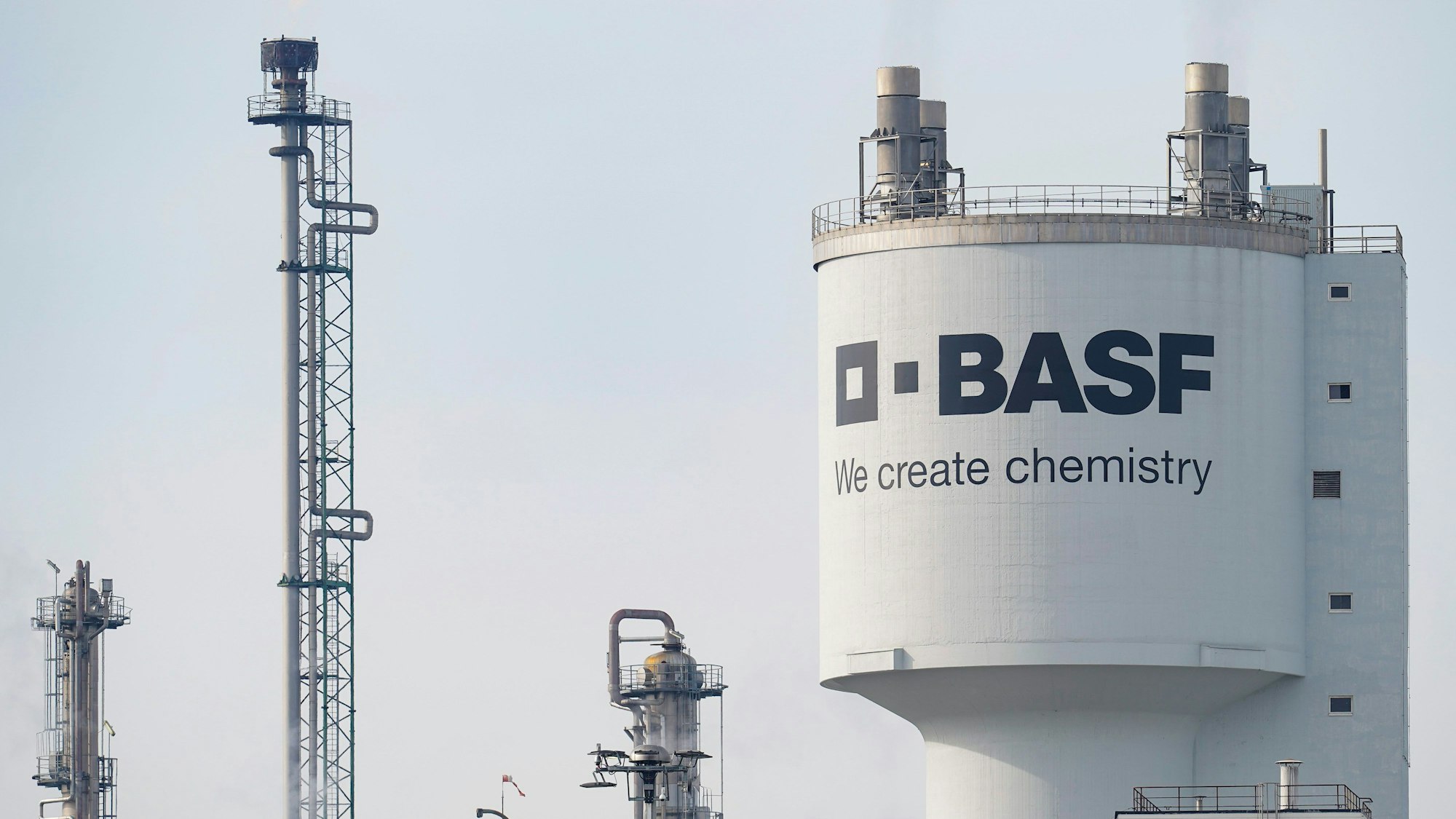 Ludwigshafen: Ein Turm mit der Aufschrift „BASF“ steht neben Schornsteinen auf dem Werksgelände des Chemiekonzerns BASF. (Archivbild)