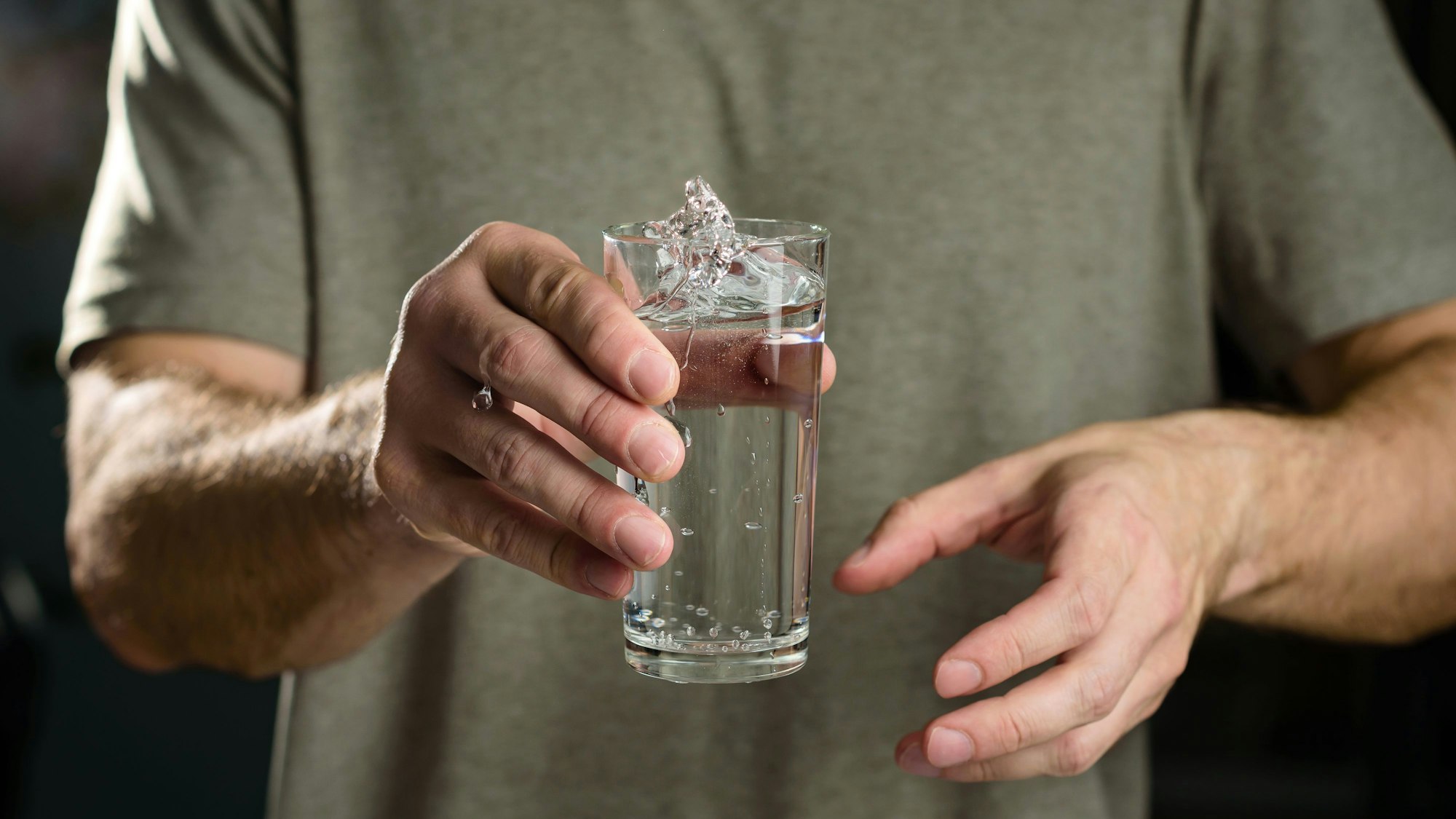 Eine Person hält ein Glas Wasser in der Hand. Das Wasser wirft kleine Wellen, was auf ein Zittern der Person hindeutet.