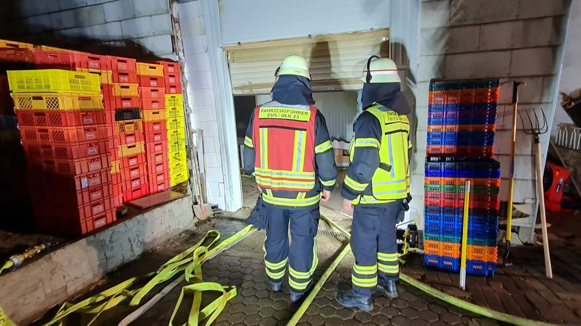 Das Bild zeigt zwei Feuerwehrleute vor einem Rolltor. Auf dem Boden liegen zahlreiche Schläuche.