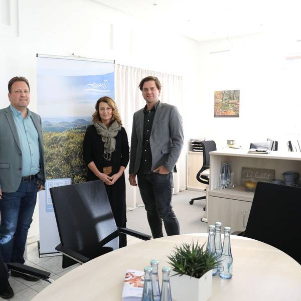 Zwei Männer und eine Frau stehen in einem Büro vor einem Tisch.