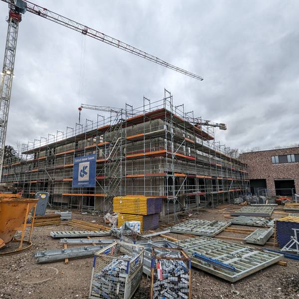 Ein eingerüsteter Rohbau mit Baumaterial und Baukran vor dem bereits fertiggestellten Gebäudetrakt der neuen Feuer- und Rettungswache.