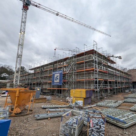 Ein eingerüsteter Rohbau mit Baumaterial und Baukran vor dem bereits fertiggestellten Gebäudetrakt der neuen Feuer- und Rettungswache.