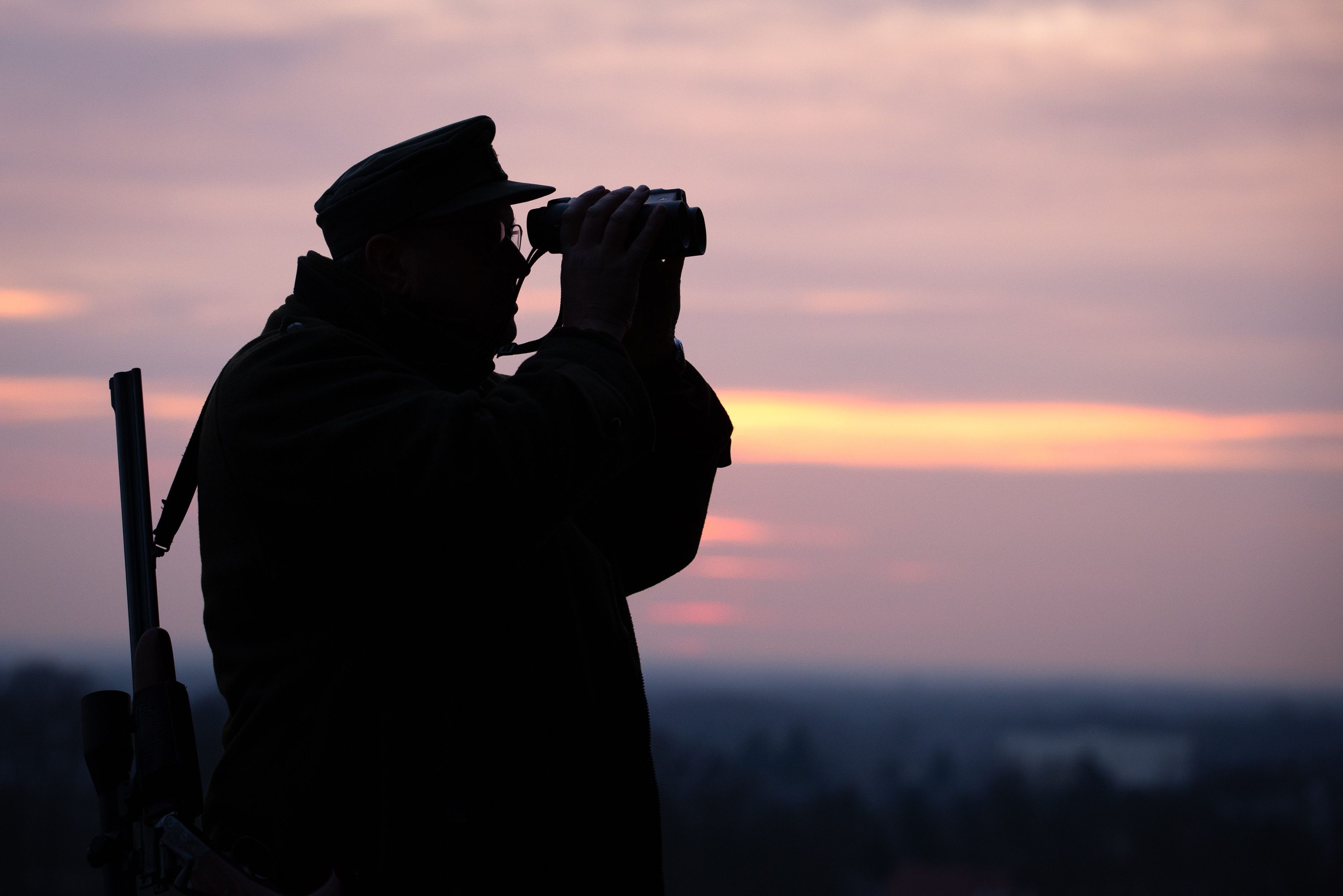 Ein Jäger blickt durch sein Fernglas in der Abenddämmerung.