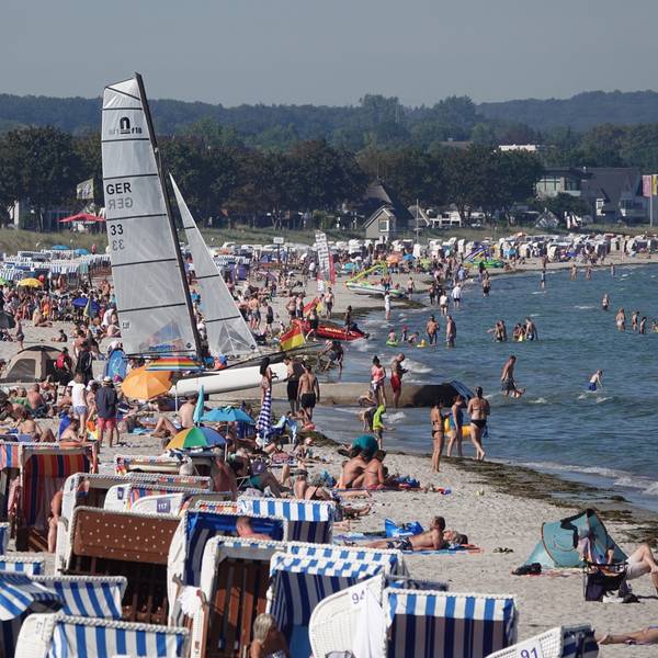Passantinnen und Passanten genießen das Sonnenwetter am Strand der Ostsee.