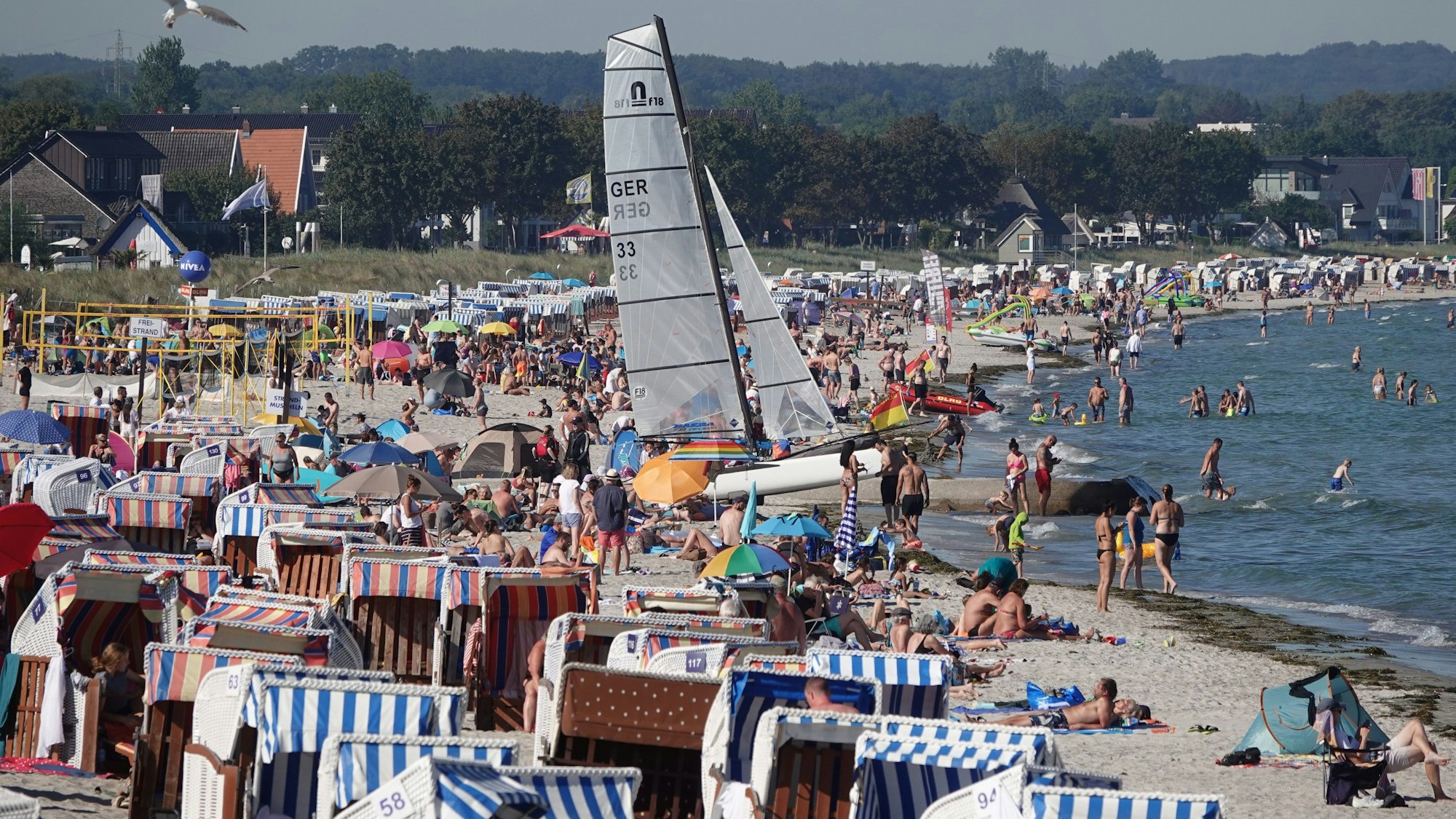 Passantinnen und Passanten genießen das Sonnenwetter am Strand der Ostsee.