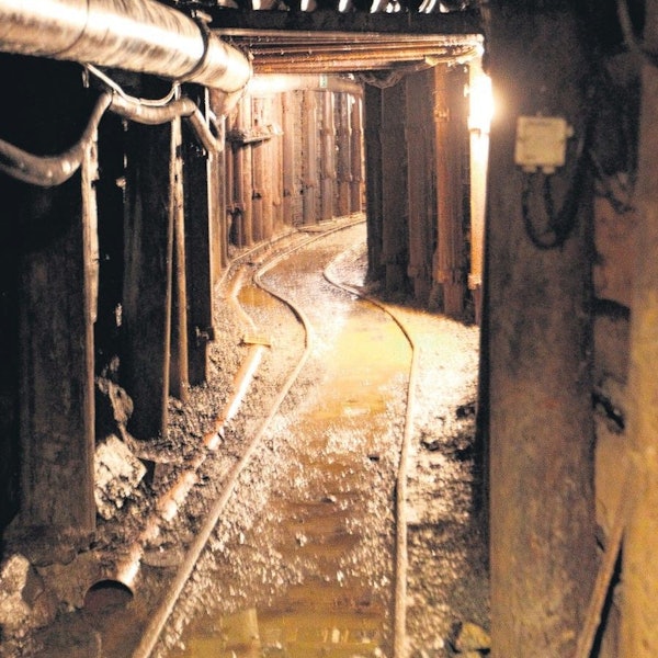 Blick in einen alten, engen Bergwerksstollen mit Schienen auf dem Boden.
