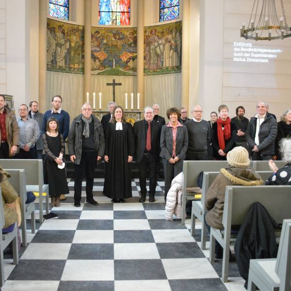 Männer und Frauen stehen vor dem Altar in der evangelischen Friedenskirche.