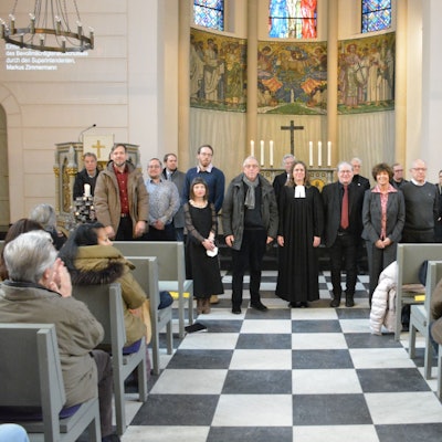 Männer und Frauen stehen vor dem Altar in der evangelischen Friedenskirche.