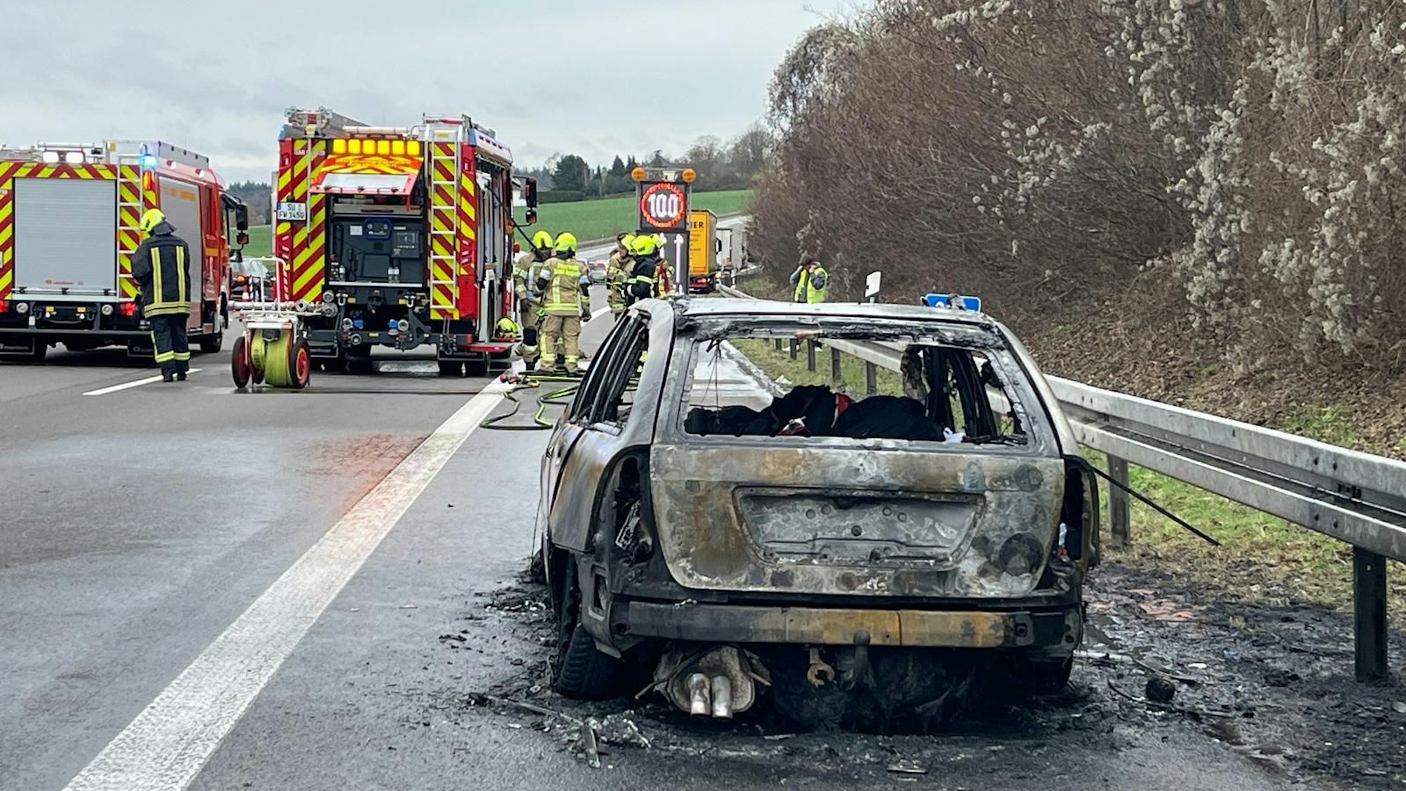 Mehrere Feuerwehrfahrzeuge stehen neben einem ausgebrannten Pkw.