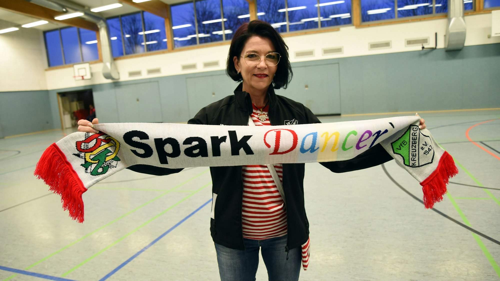 Tanztrainerin Alex Jesinghaus hält einen Schal in den Händen. Darauf steht in bunten Buchstanden „Spark Dancers“.