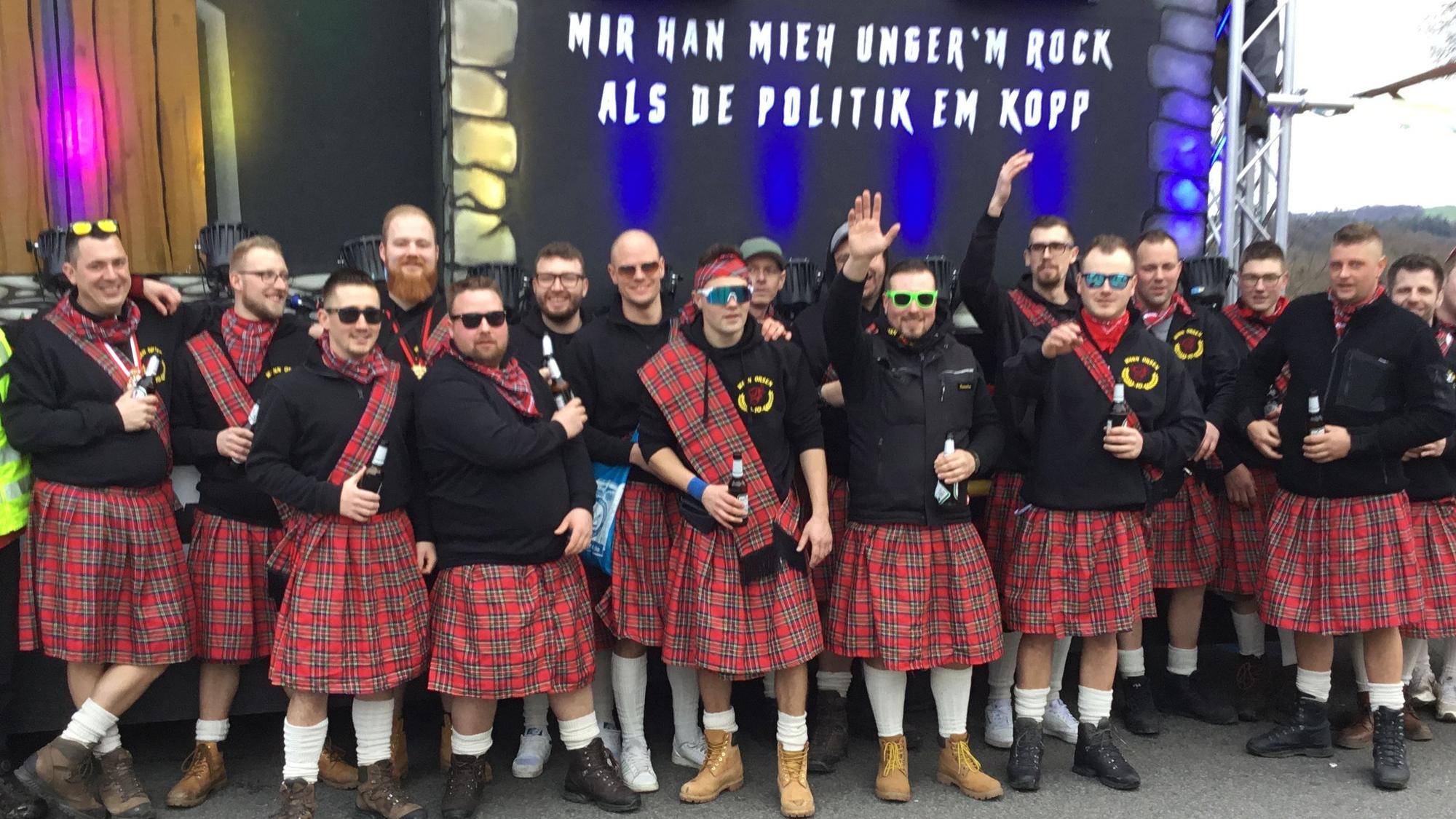 Eine Gruppe steht in Schottenröcken vor einer Halle.