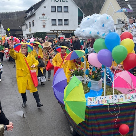 Eine mit Regenjacken und Schirmen auf dem Kopf verkleidete Gruppe, verteilt beim Karnevalszug in Gummersbach-Rebbelroth Kamelle.