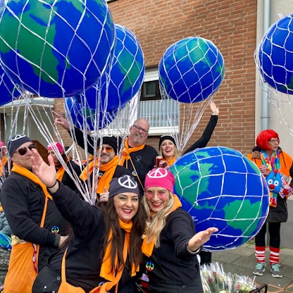 Eine Gruppe von Männern und Frauen mit orangefarbenen Schals, großen Ballons und Kopftüchern mit dem Friedenszeichen.