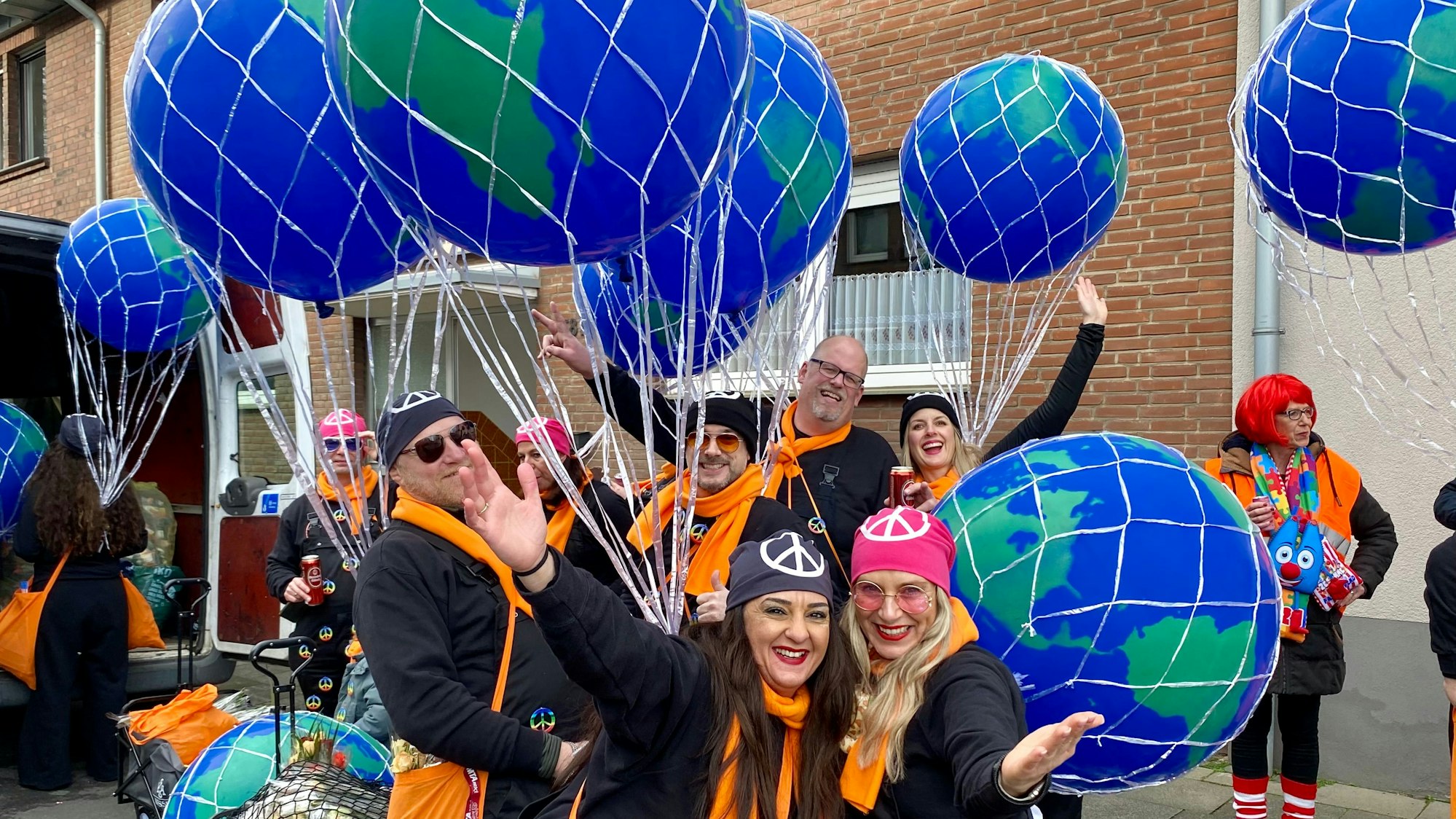 Eine Gruppe von Männern und Frauen mit orangefarbenen Schals, großen Ballons und Kopftüchern mit dem Friedenszeichen.