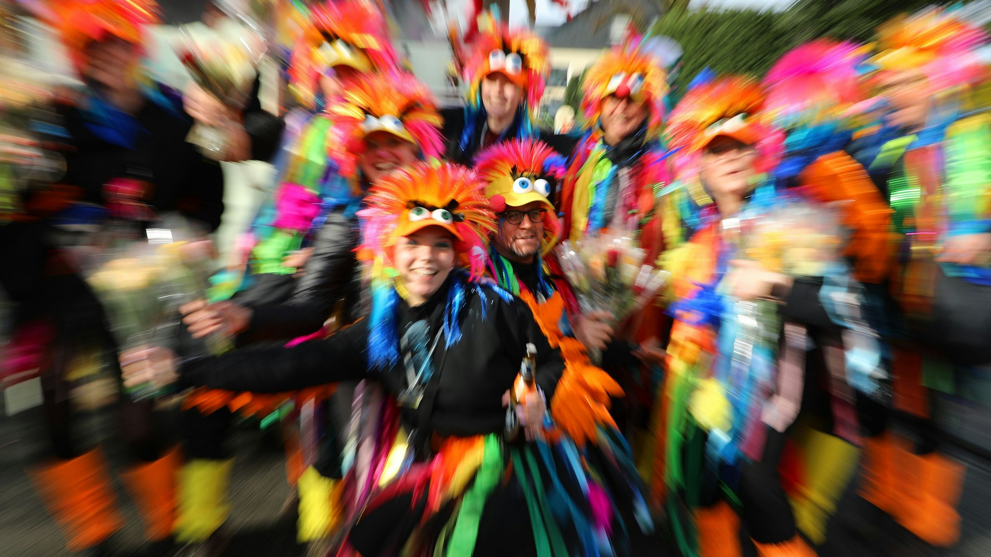 Menschen in Papageienkostümen stehen als Gruppe zusammen. Die Kamera zoomt schnell in das Bild hinein, dadurch kommt es zu Wischeffekten.