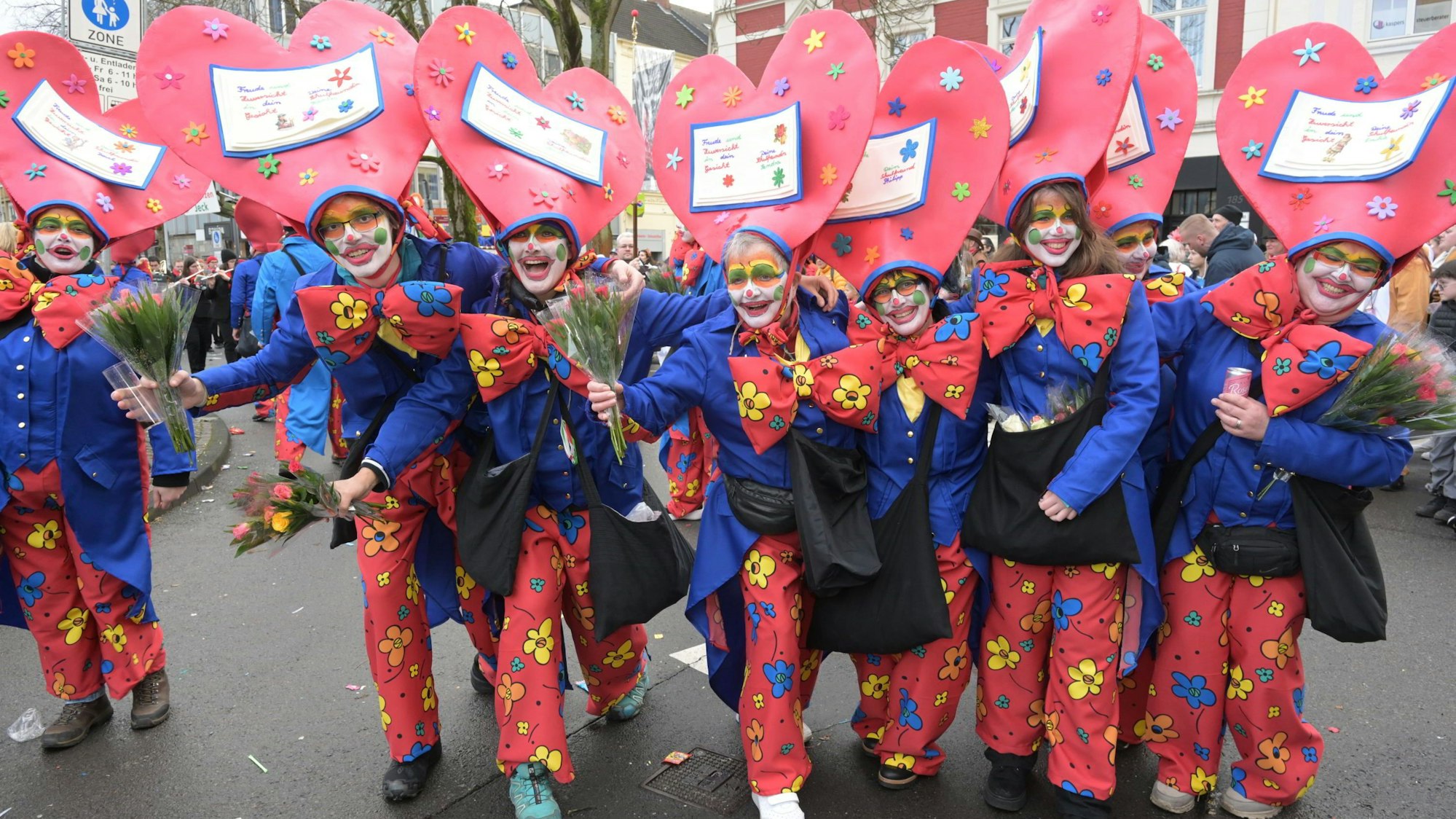 Menschen mit Herzhüten stehen in einer Reihe.