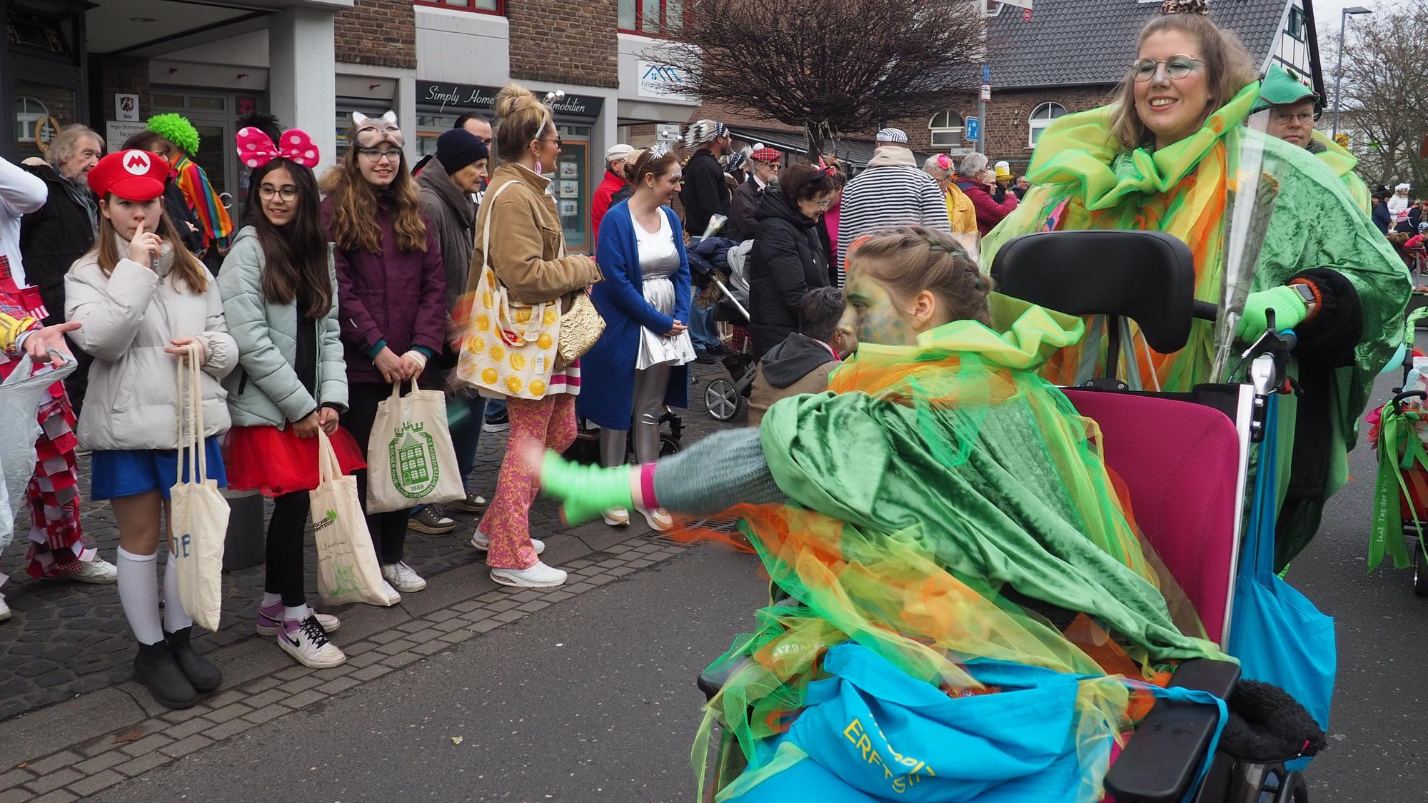 Ein bunt kostümiertes Mädchen sitzt im Rollstuhl und verteilt Süßigkeiten.