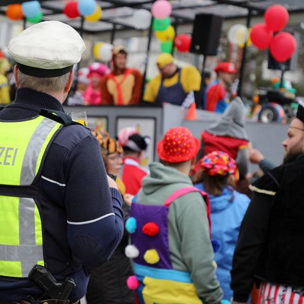 Ein Polizist steht an einem Karnevalszug und beobachtet das jecke Treiben.