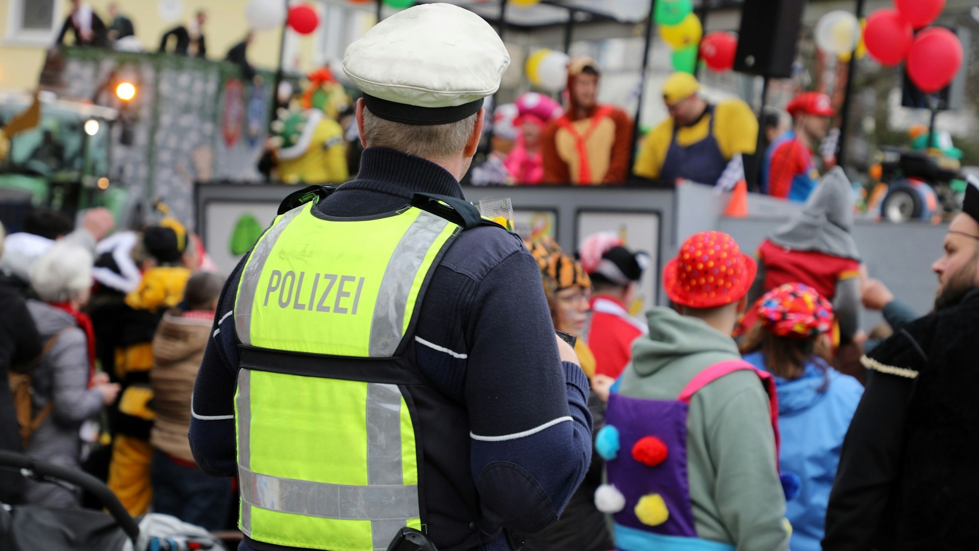 Ein Polizist steht an einem Karnevalszug und beobachtet das jecke Treiben.