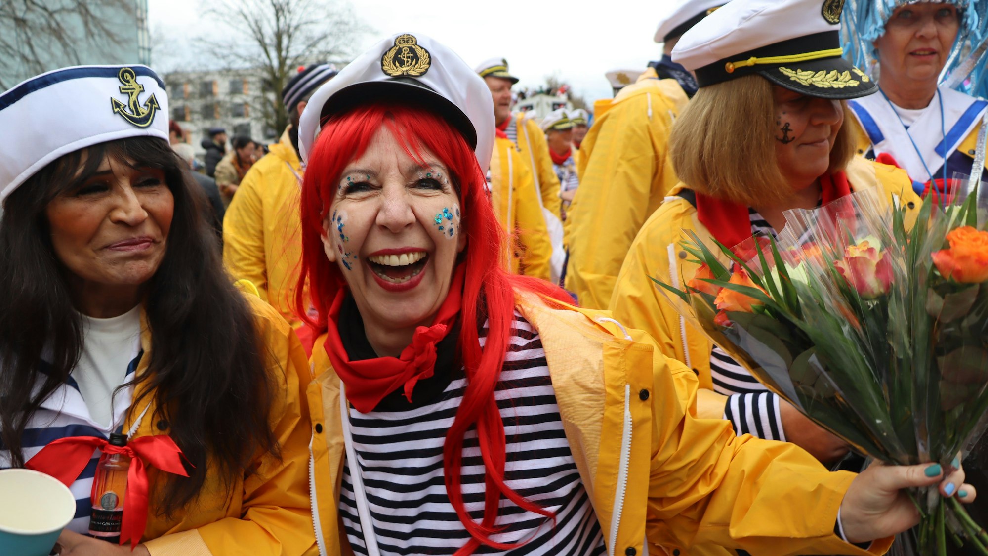 Eine strahlende Frau im Kapitänskostüm verteilt mit ihrer Gruppe Blumensträuße.