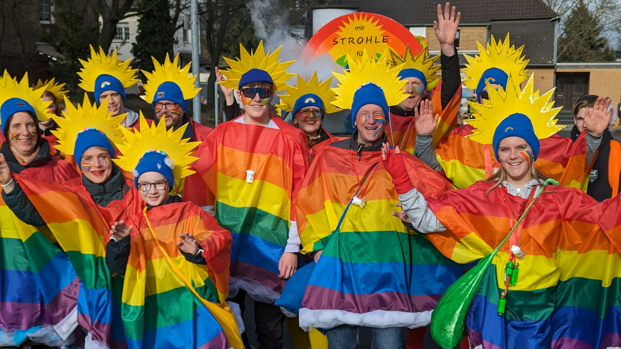 Eine Gruppe von Männern und Frauen mit Regenbogen-Umhängen und Strahlenkronen auf dem Kopf.