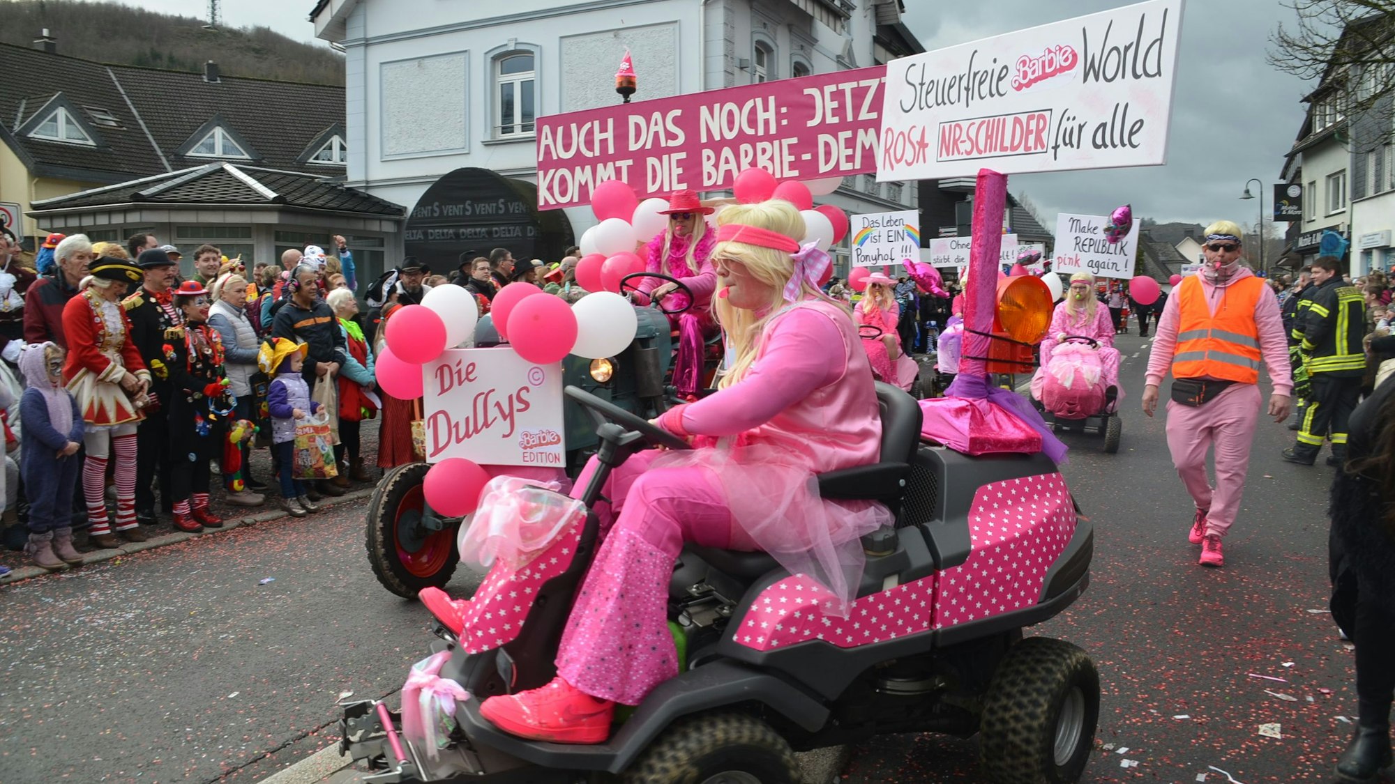 Als Barbie verkleidete Jecke sind bei einem Umzug auf rosafarbenen Sitzrasenmähern unterwegs.