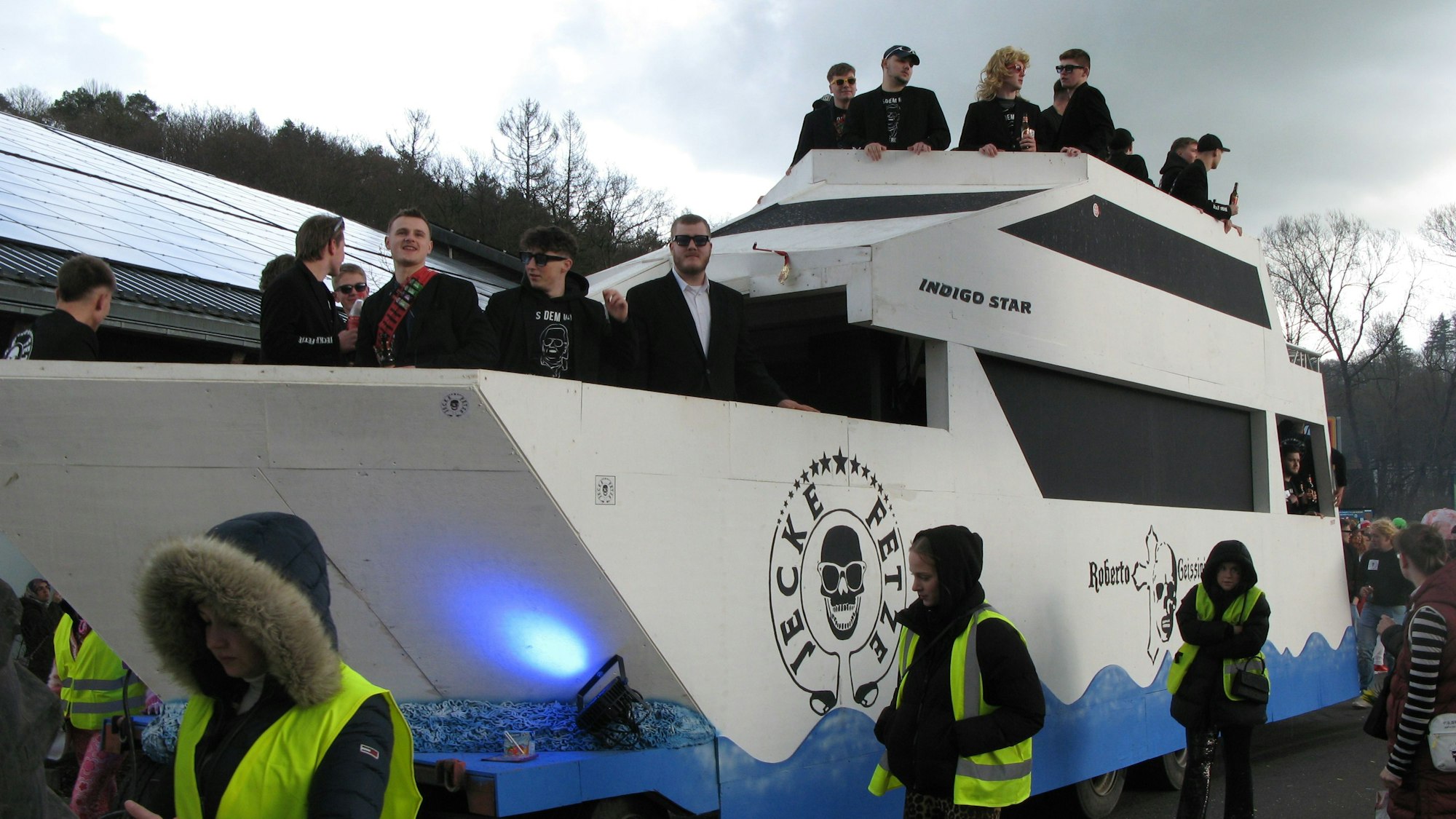 Junge Leute in schwarzer Kleidung auf einem Zugwagen, der wie eine große Motoyacht aussieht.