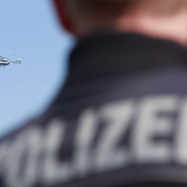 Ein Polizeihubschrauber fliegt am Himmel, im Vordergrund steht ein Polizist.
