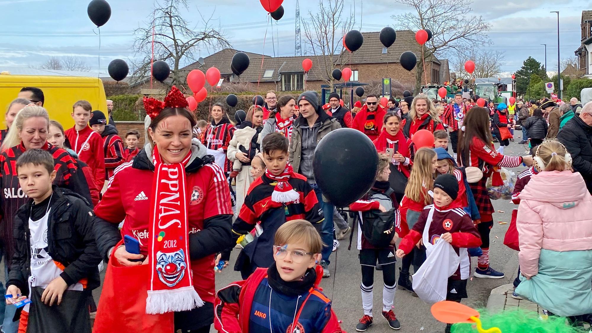 Kinder und Jugendliche in Fußballtrikots und mit schwarzen und roten Ballons in den Händen.