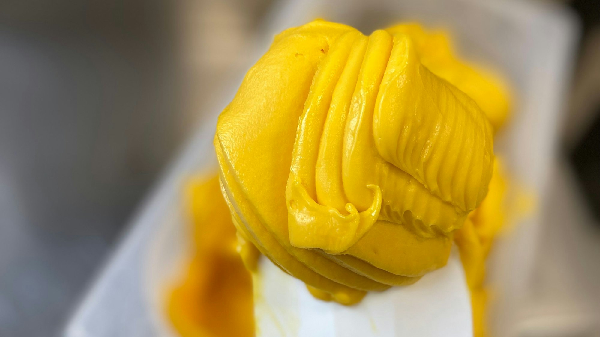 Auf einem Löffel ist ein gelb-orange farbenes Eis zu sehen.