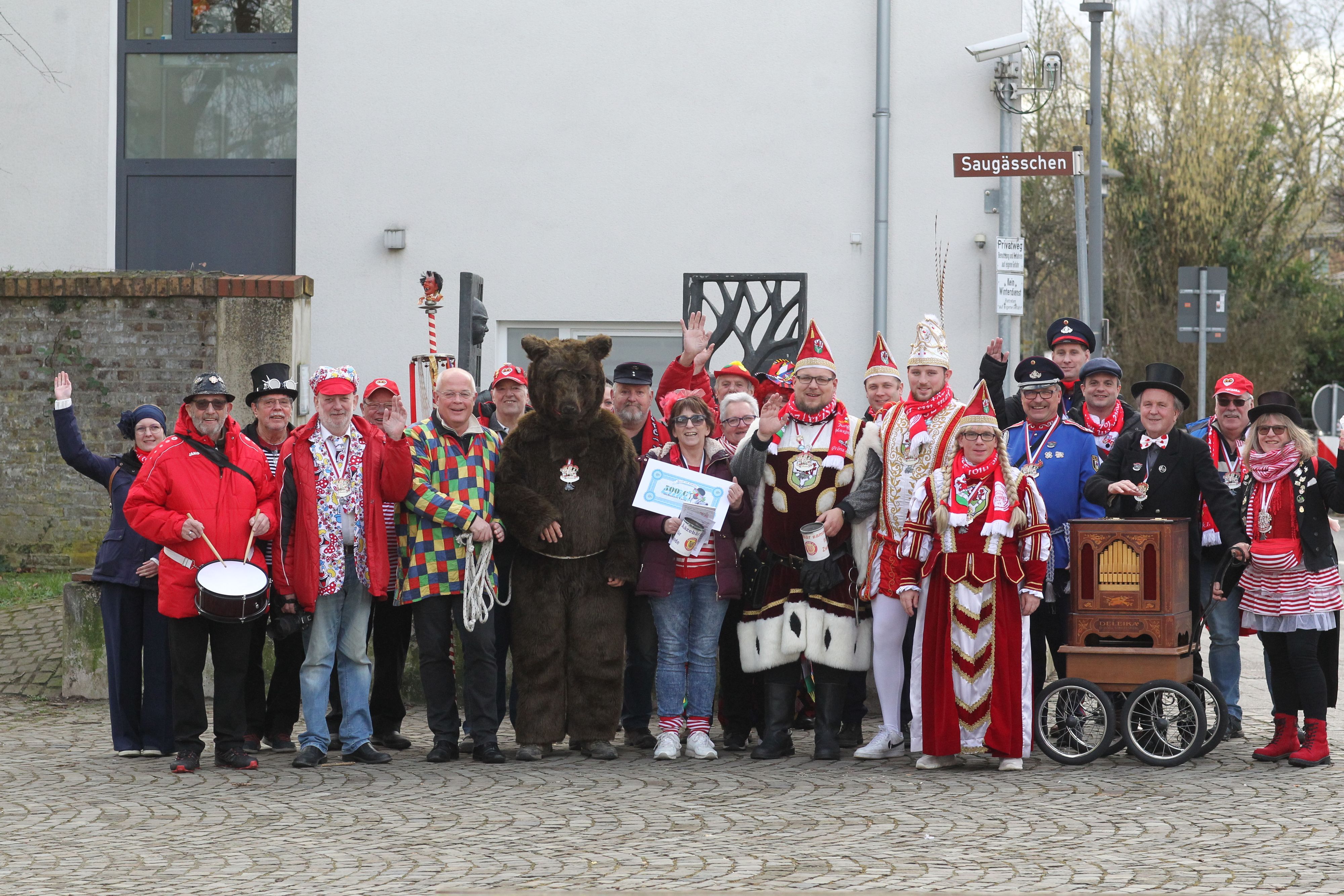 Eine Gruppe von etwa 25 Leuten, darunter der Ääzebär in einem dunkelbraunem Fellkostüm, ein Mann mit Drehorgel, ein Trommler und das Lohmarer Dreigestirn.