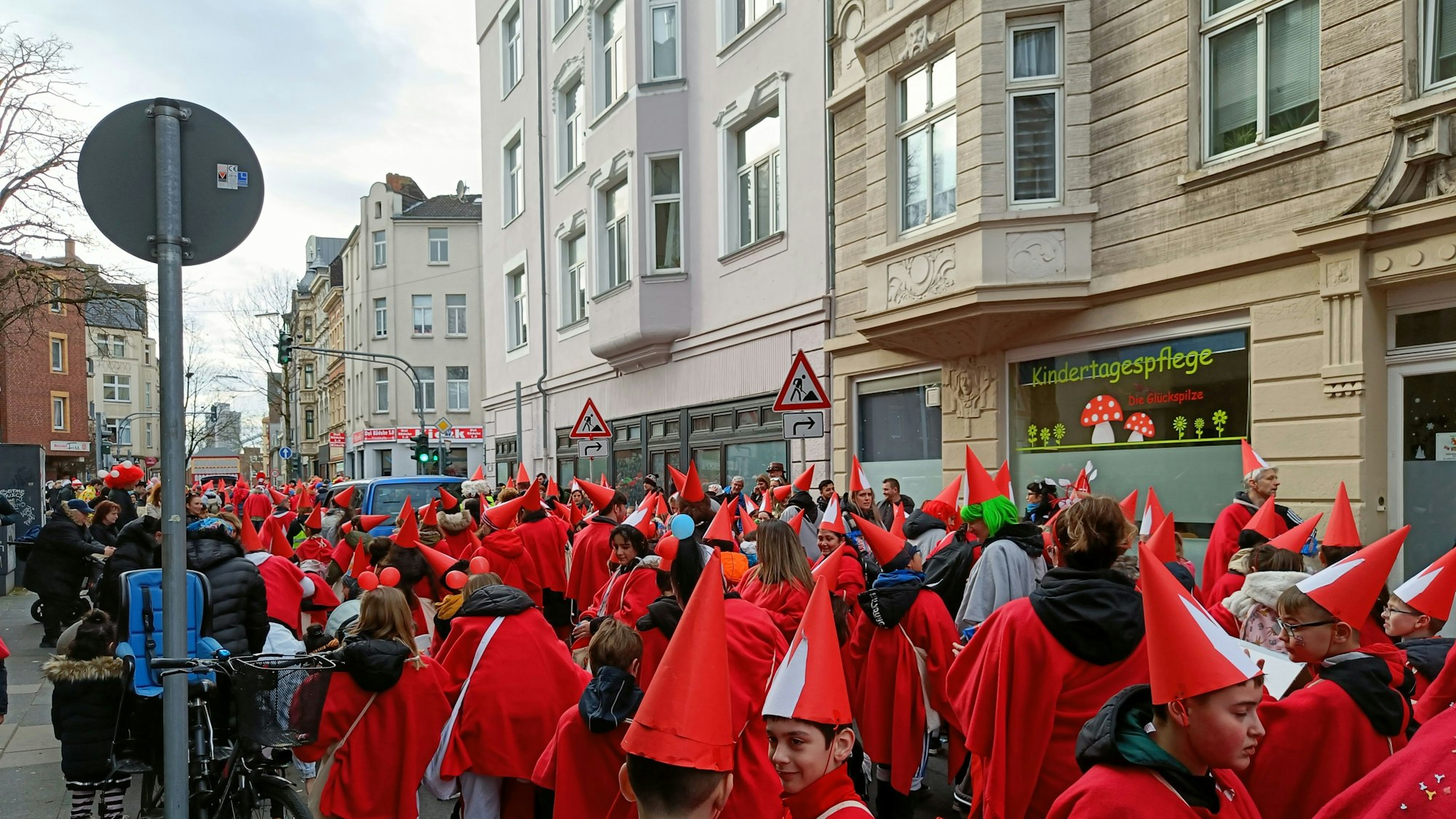 Kinder in roten Kostümen und Spitzhüten stehen als Teil des Veedelszugs auf einer Mülheimer Straße.
