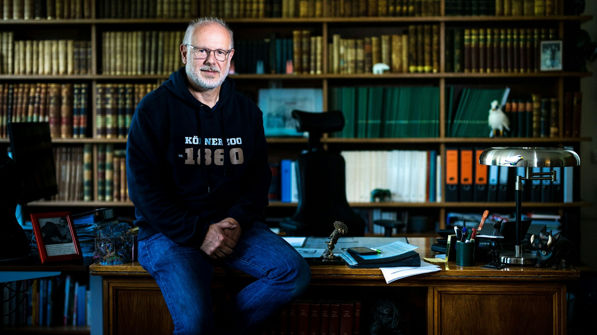 Kölns Zoodirektor Theo Pagel sitzt auf der Kante seines Schreibtischs.