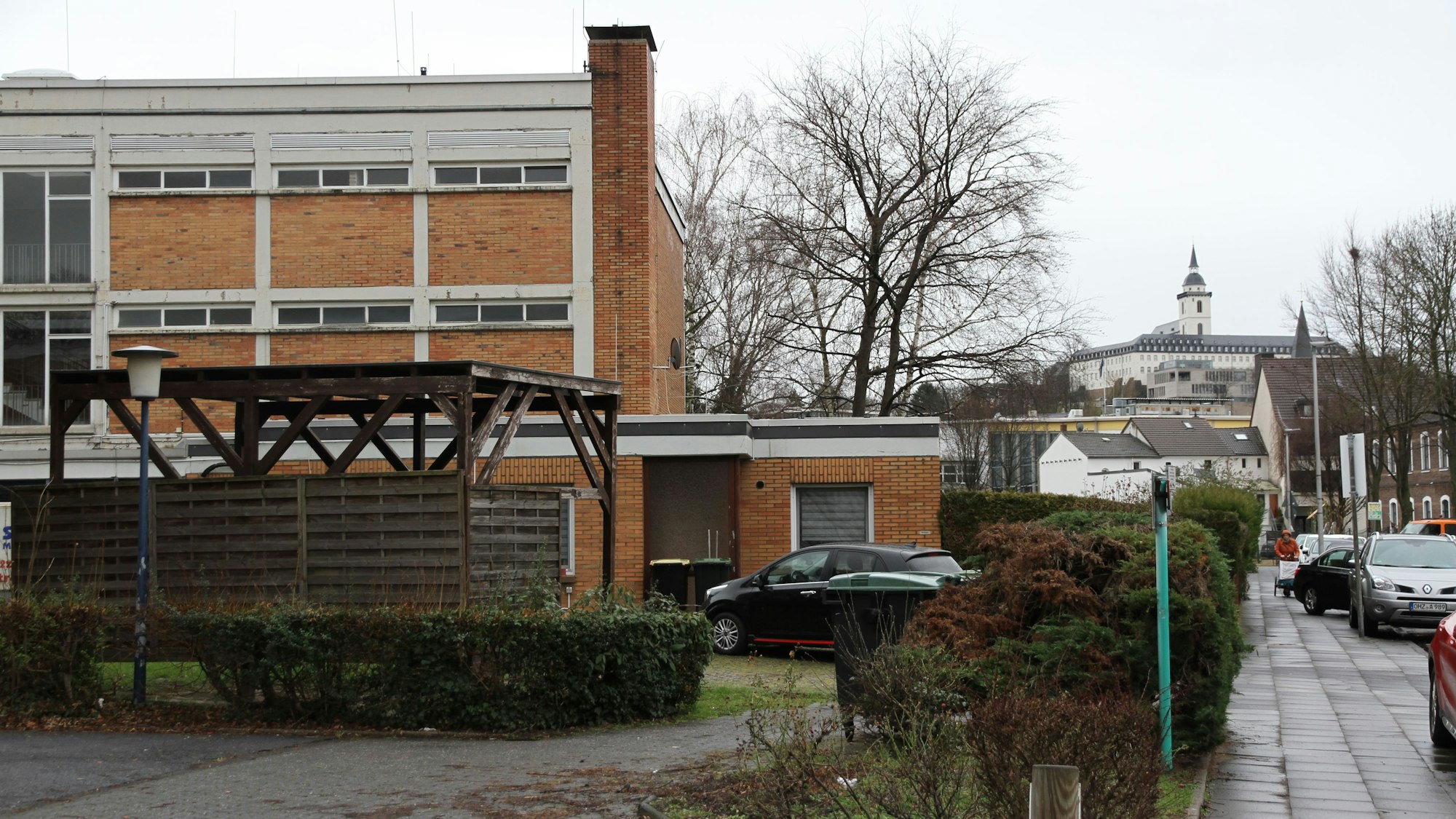 Ein verklinkertes Schulgebäude, im Hintergrund ein Berg mit einem Kloster und Kirchturm