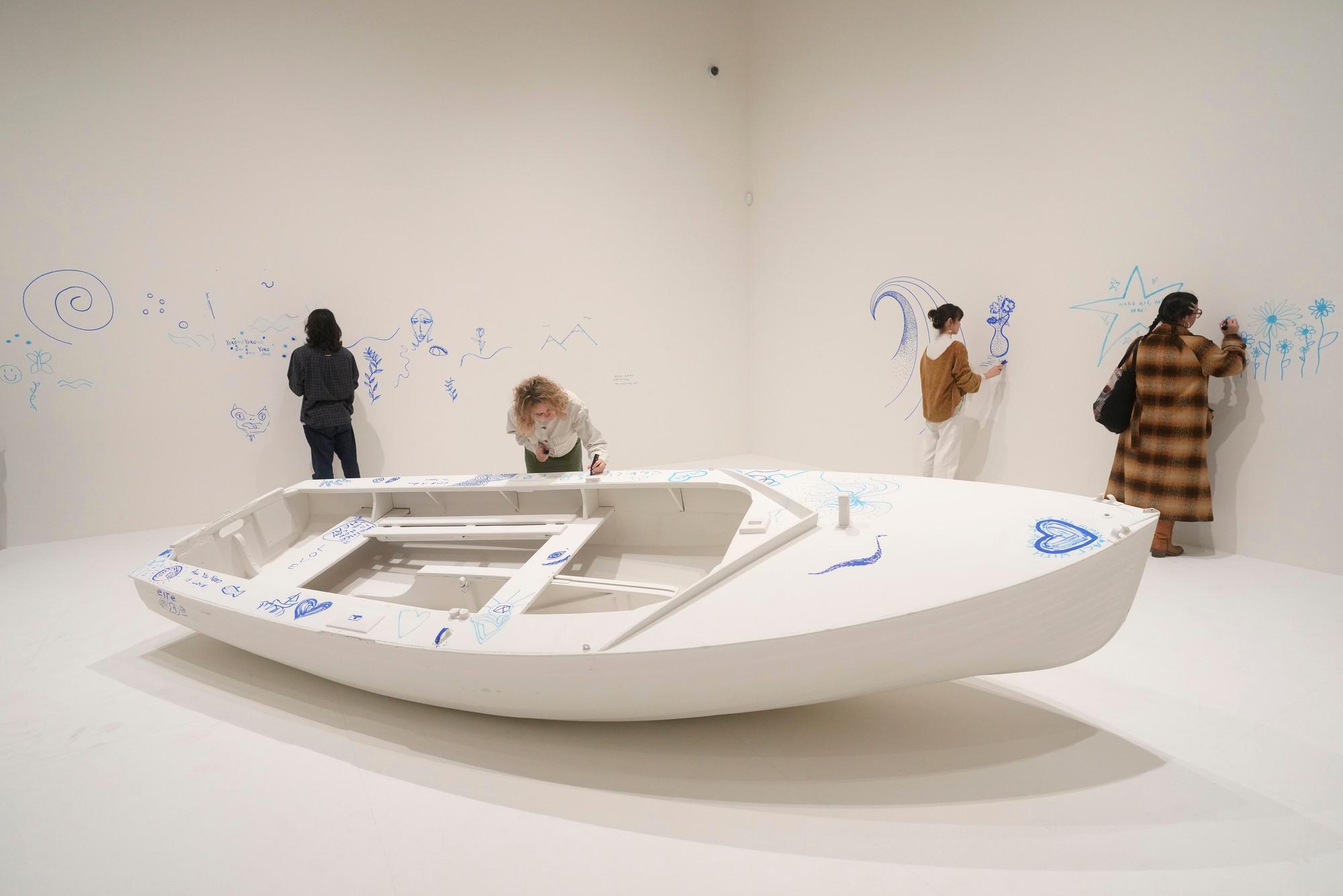 Members of staff draw on a work entitled Add Colour (Refugee Boat), Concept 1960, first realised 2016, exhibition realisation 2024, at the Yoko Ono : Music of the Mind exhibition at the Tate Modern, the works of art are copyright Yoko Ono, In London, Tuesday, Feb. 13, 2024. The exhibition which has many pieces that are interactive and the public and which participate in, runs from Feb.15, to Sept. 1. (AP Photo/Alastair Grant)